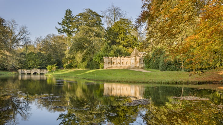 Looking across a still body of water towards the Temple of British Worthies and the Shell Bridge at at Stowe, Buckinghamshire.